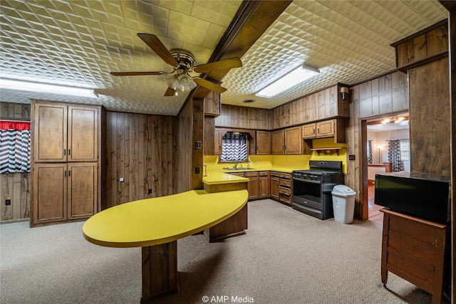 kitchen with gas range, ceiling fan, wooden walls, and light carpet