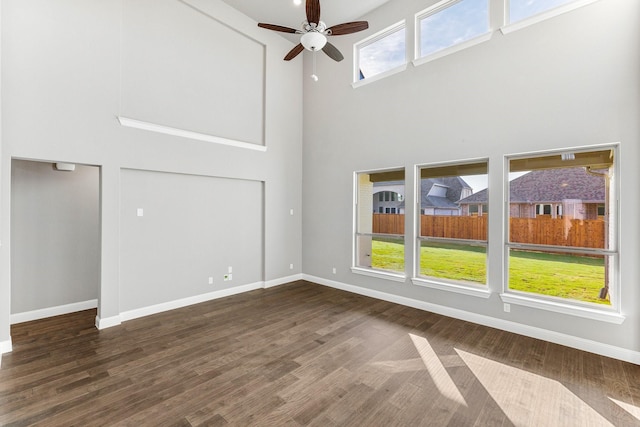 unfurnished living room with a high ceiling, dark wood-type flooring, and ceiling fan