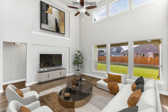 living room featuring hardwood / wood-style floors, a towering ceiling, a fireplace, and ceiling fan