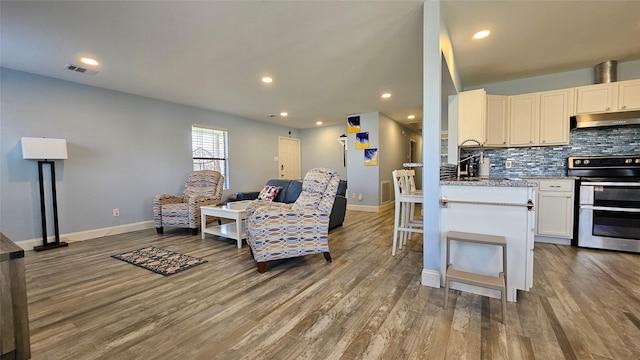 kitchen with double oven range, wood-type flooring, white cabinets, and decorative backsplash