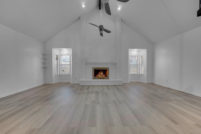 unfurnished living room with ceiling fan, beam ceiling, high vaulted ceiling, a brick fireplace, and light wood-type flooring