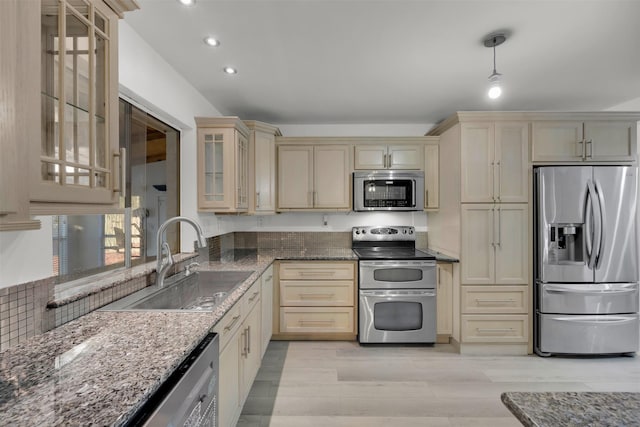 kitchen with pendant lighting, sink, light hardwood / wood-style flooring, appliances with stainless steel finishes, and dark stone countertops