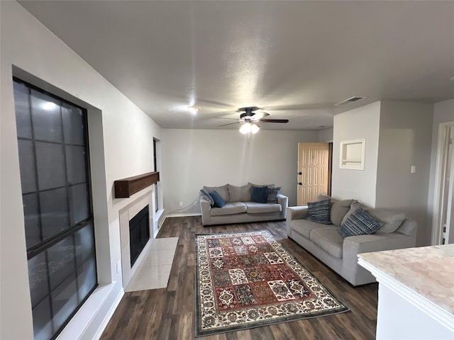 living room with a fireplace, dark wood-type flooring, and ceiling fan