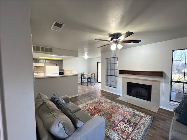 living room featuring dark wood-type flooring, ceiling fan, and a tiled fireplace