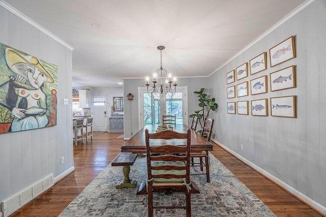 dining space with dark wood-type flooring, ornamental molding, and a chandelier