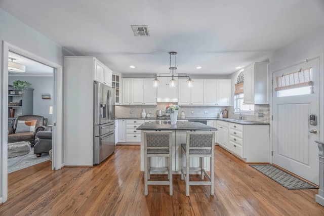 kitchen with white cabinets, a kitchen bar, hanging light fixtures, a center island, and stainless steel refrigerator with ice dispenser