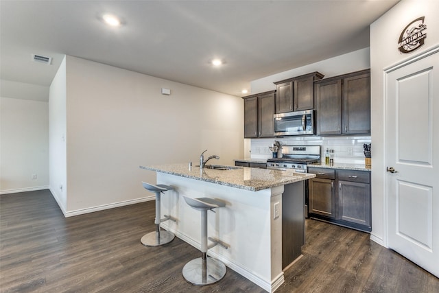 kitchen with appliances with stainless steel finishes, tasteful backsplash, sink, dark brown cabinets, and a center island with sink