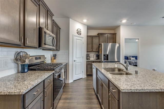 kitchen with dark wood-type flooring, sink, tasteful backsplash, stainless steel appliances, and a kitchen island with sink