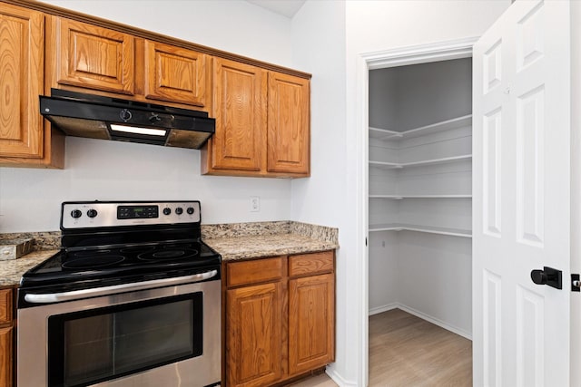 kitchen featuring stainless steel electric range, light hardwood / wood-style flooring, and light stone countertops