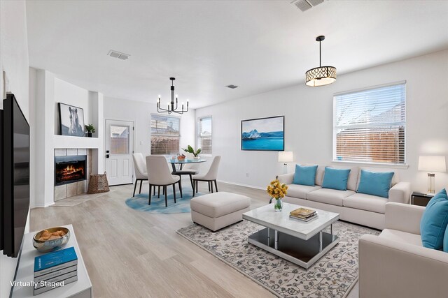 unfurnished living room with a tiled fireplace, a chandelier, and light wood-type flooring