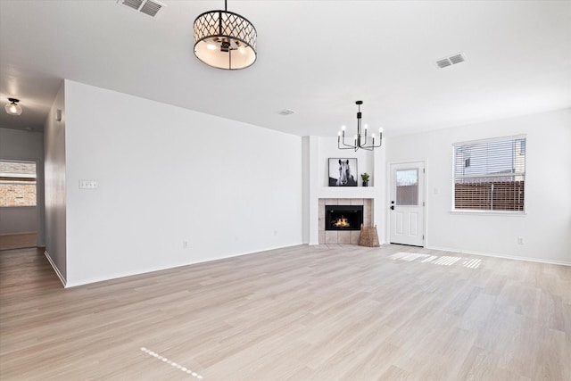 unfurnished living room with a tiled fireplace, a healthy amount of sunlight, and light wood-type flooring