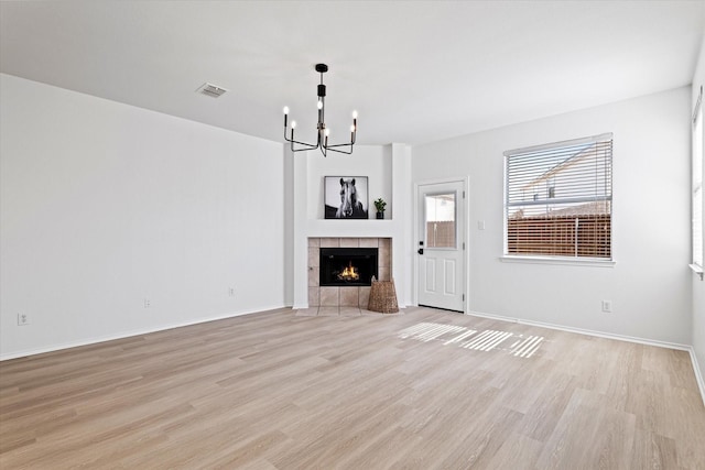 unfurnished living room with an inviting chandelier, a tiled fireplace, and light hardwood / wood-style floors