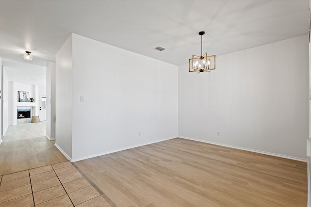 unfurnished room with a tiled fireplace, light hardwood / wood-style flooring, and an inviting chandelier