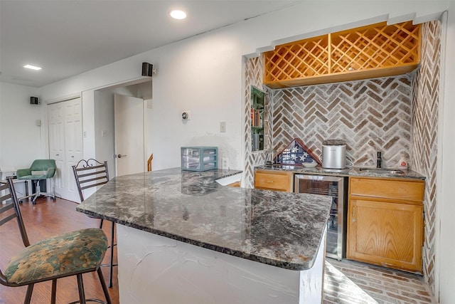 kitchen featuring sink, a kitchen breakfast bar, tasteful backsplash, beverage cooler, and dark stone counters