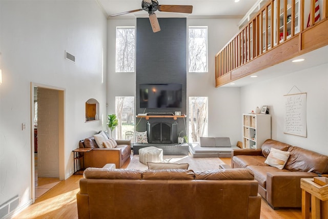 living room with a fireplace, a high ceiling, ceiling fan, light hardwood / wood-style floors, and crown molding