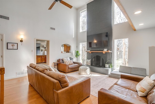 living room with a high ceiling, ceiling fan, a fireplace, and light hardwood / wood-style floors