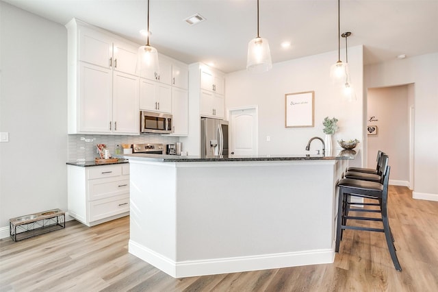 kitchen with pendant lighting, stainless steel appliances, tasteful backsplash, white cabinets, and a center island with sink