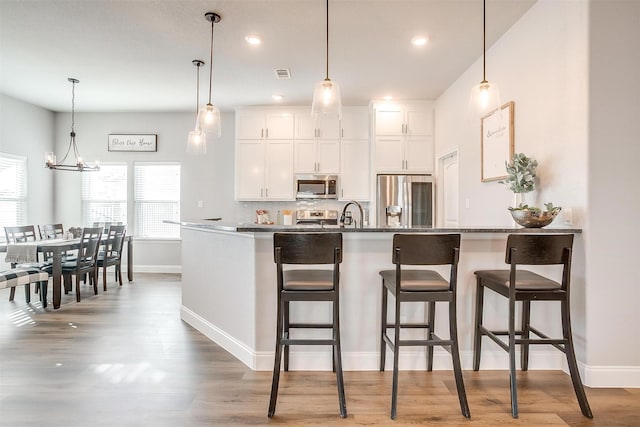 kitchen featuring white cabinetry, decorative light fixtures, stainless steel appliances, and dark stone countertops