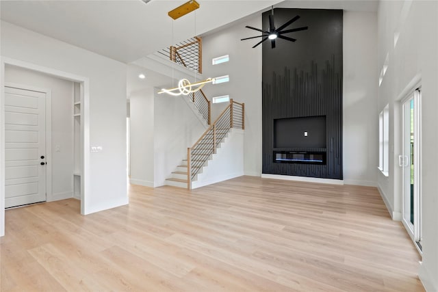 unfurnished living room with a towering ceiling, ceiling fan with notable chandelier, a fireplace, and light hardwood / wood-style floors