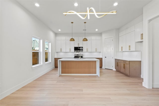 kitchen with hanging light fixtures, white cabinetry, a center island with sink, and light hardwood / wood-style floors