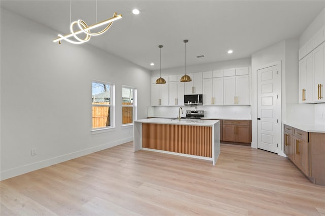 kitchen with appliances with stainless steel finishes, hanging light fixtures, a center island with sink, and white cabinets