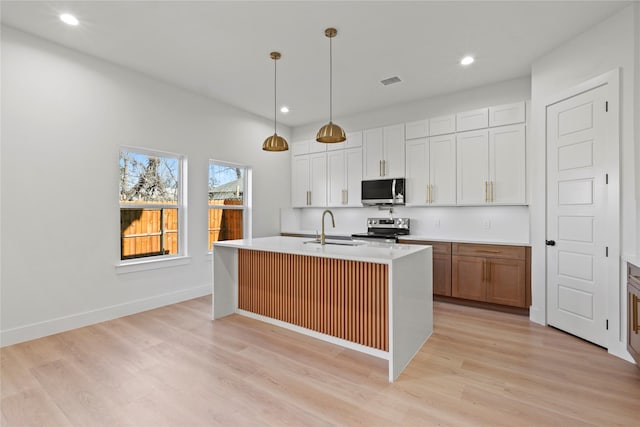 kitchen with decorative light fixtures, an island with sink, sink, white cabinets, and stainless steel appliances