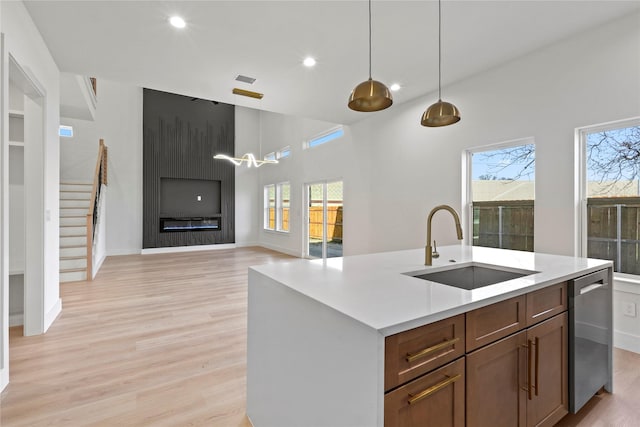 kitchen featuring pendant lighting, sink, stainless steel dishwasher, light hardwood / wood-style floors, and a center island with sink