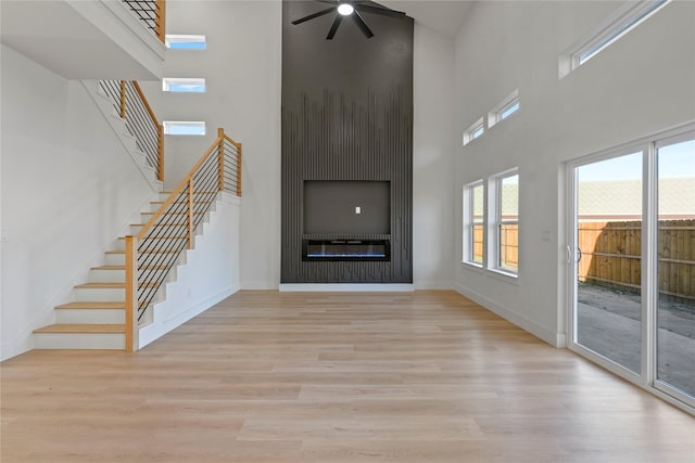 unfurnished living room featuring ceiling fan, a large fireplace, light hardwood / wood-style flooring, and a high ceiling