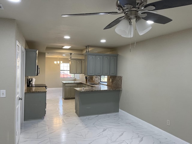 kitchen featuring sink, gray cabinetry, kitchen peninsula, ceiling fan with notable chandelier, and decorative backsplash