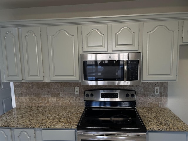 kitchen featuring white cabinetry, stainless steel appliances, decorative backsplash, and dark stone counters