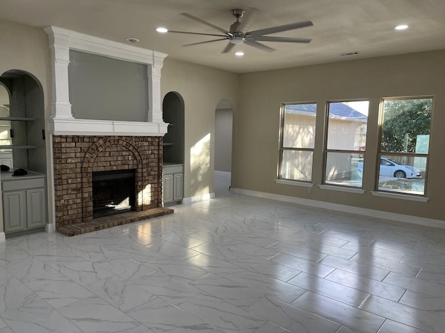 unfurnished living room with a brick fireplace, built in shelves, and ceiling fan