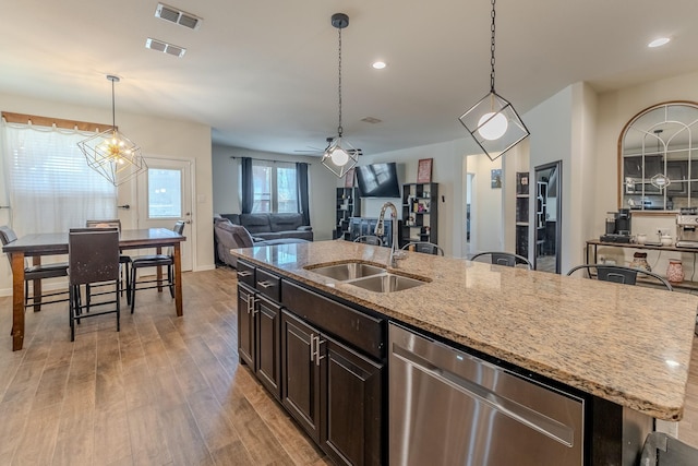 kitchen with dishwasher, an island with sink, sink, hanging light fixtures, and light stone countertops