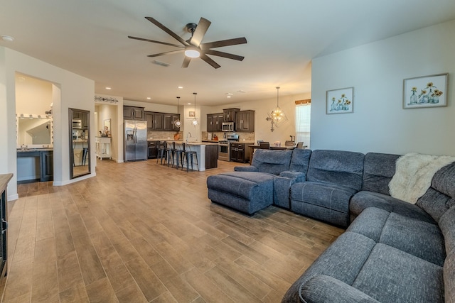 living room with sink, ceiling fan with notable chandelier, and light hardwood / wood-style flooring