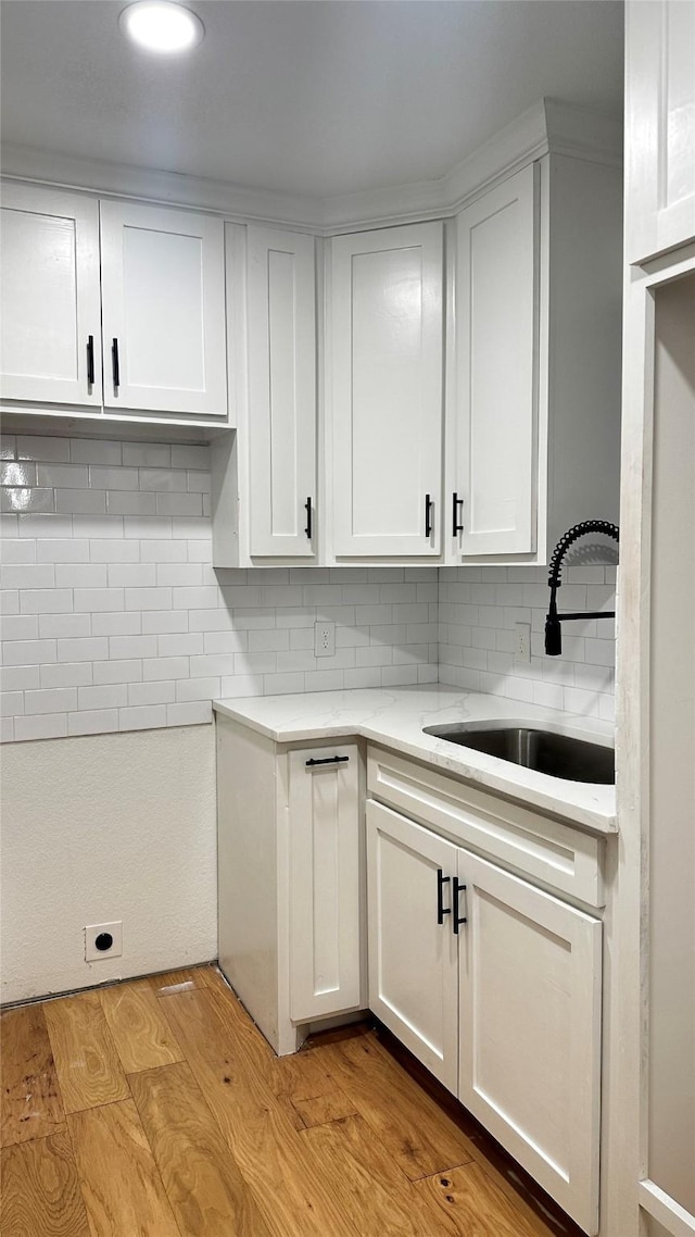 kitchen with tasteful backsplash, sink, white cabinets, and light hardwood / wood-style floors