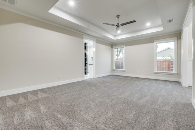 empty room with crown molding, ceiling fan, a raised ceiling, and carpet