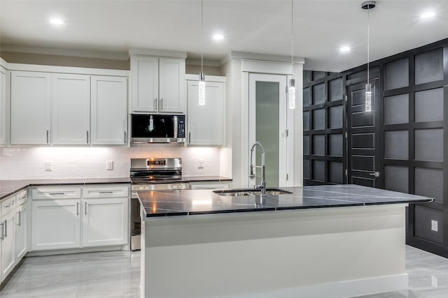 kitchen featuring appliances with stainless steel finishes, an island with sink, white cabinetry, sink, and hanging light fixtures