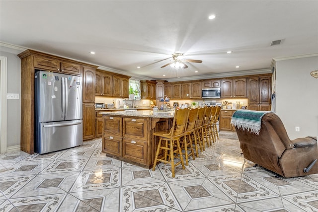 kitchen with a breakfast bar, stainless steel appliances, a center island, light stone countertops, and ornamental molding