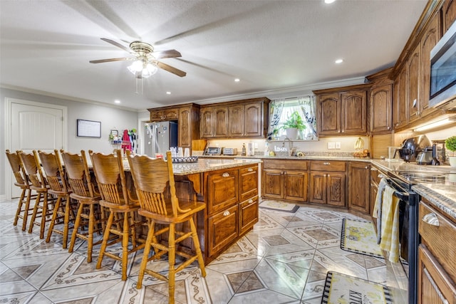 kitchen with a breakfast bar area, ornamental molding, appliances with stainless steel finishes, a kitchen island, and light stone countertops