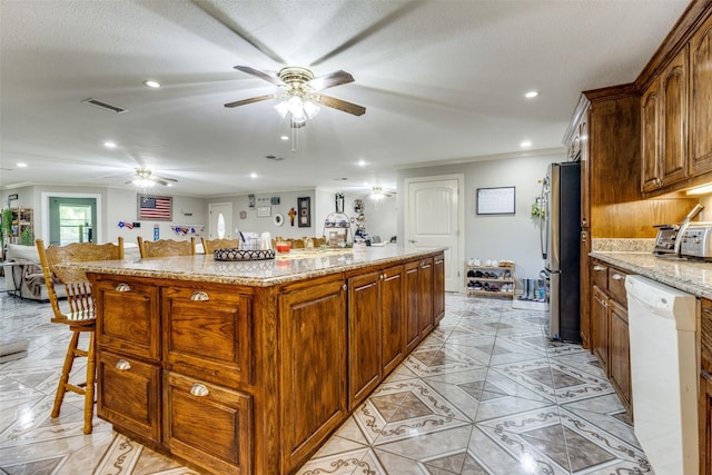 kitchen featuring a kitchen bar, light stone counters, stainless steel fridge, dishwasher, and a kitchen island