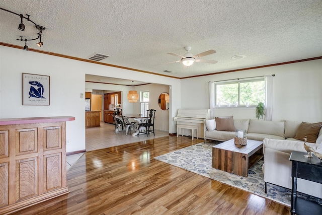 living area featuring light wood-type flooring, visible vents, ornamental molding, and a healthy amount of sunlight