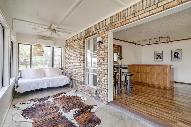 bedroom featuring a wall unit AC, a bar, brick wall, rail lighting, and ornamental molding