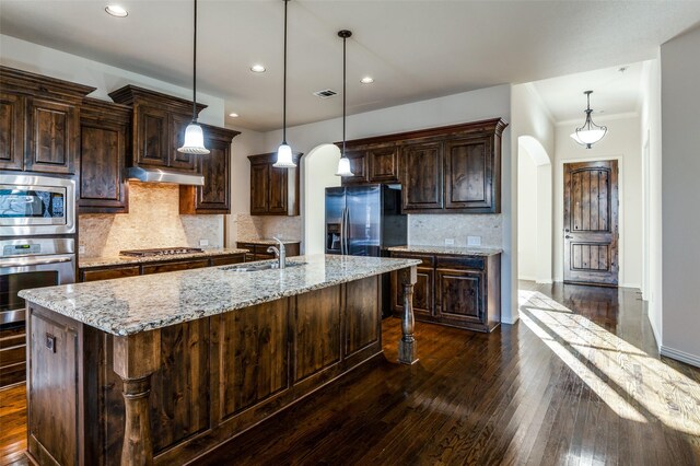 kitchen with hanging light fixtures, appliances with stainless steel finishes, and a kitchen island with sink