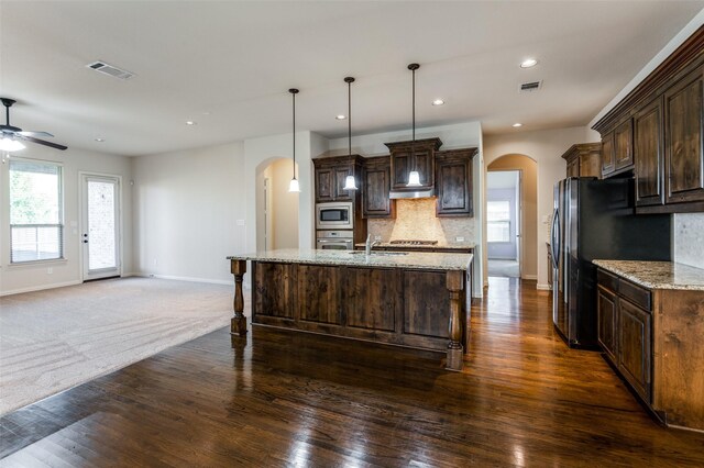 kitchen featuring dark brown cabinetry, sink, light stone counters, decorative light fixtures, and an island with sink