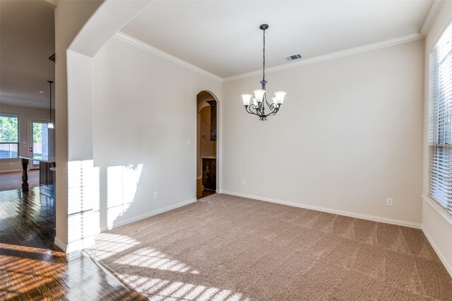 carpeted empty room with crown molding, plenty of natural light, and a chandelier