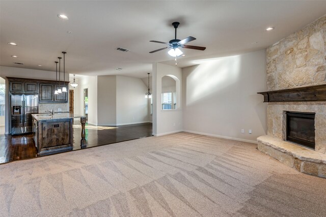 unfurnished living room featuring a stone fireplace, carpet floors, and ceiling fan