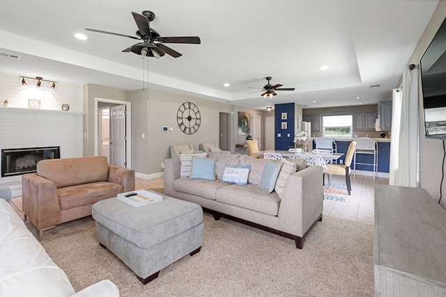 living room with a raised ceiling, ceiling fan, light tile patterned floors, and a fireplace