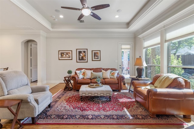 living room with hardwood / wood-style floors, a tray ceiling, ornamental molding, and ceiling fan