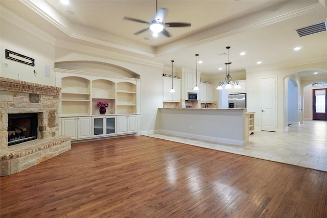 unfurnished living room featuring ornamental molding, a stone fireplace, ceiling fan, and light hardwood / wood-style floors