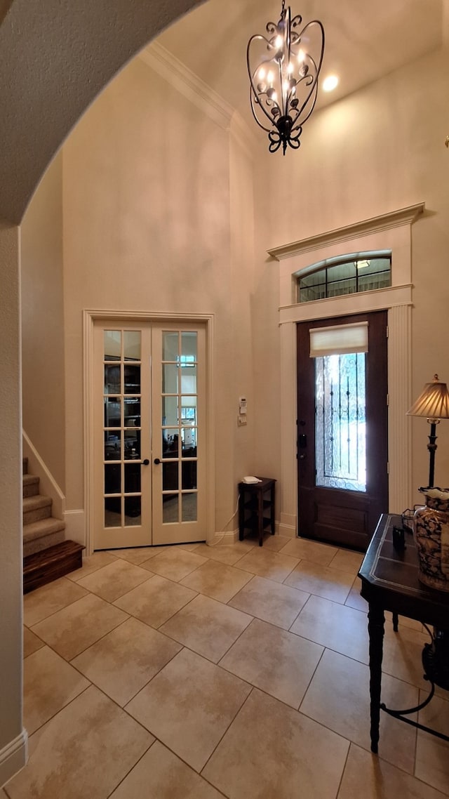 tiled foyer entrance with crown molding, french doors, a chandelier, and a towering ceiling