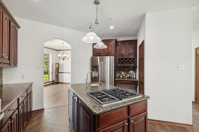 kitchen with sink, hanging light fixtures, dark stone counters, stainless steel appliances, and a kitchen island with sink